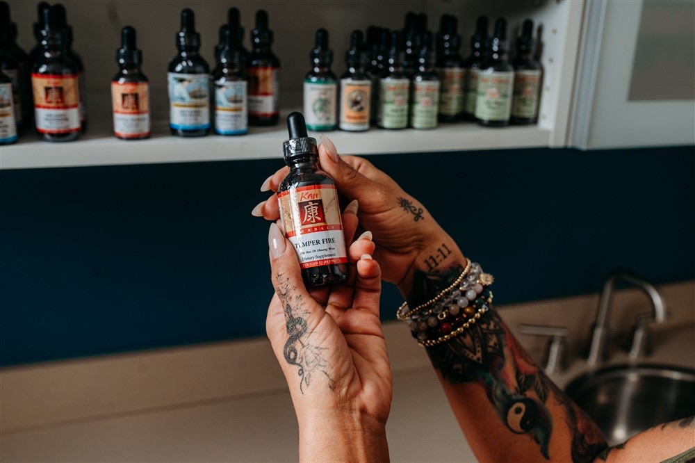 Christina holding an herbal tincture in front of the herb shelf